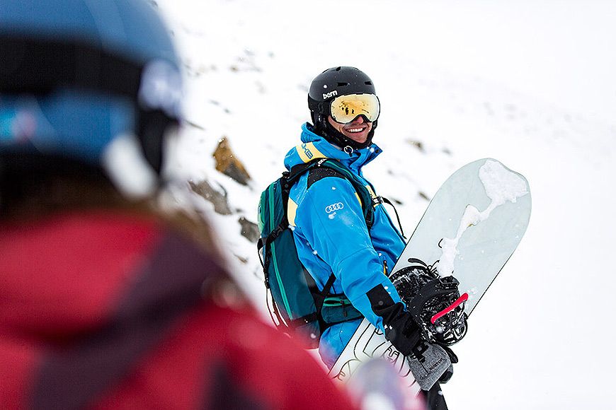 Mann in Snowboard-Outfit trägt sein Snowboard in der Hand
